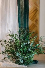 The decor of flowers and greenery for a wedding in a restaurant. The wedding arch is decorated with white and green textile fabric. Close up.