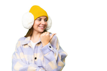 Young blonde woman wearing winter muffs over isolated chroma key background pointing to the side to...