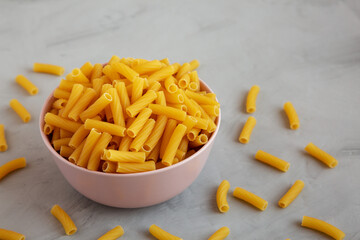 Dry Rigatoni Pasta in a Pink Bowl on a gray background, side view.