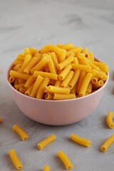 Dry Rigatoni Pasta in a Pink Bowl on a gray background, side view.