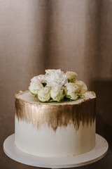 Wedding cake with white flowers for a banquet. Delicious reception. Copy space. Celebration party concept. Trendy golden cake with gold decor. Close up.