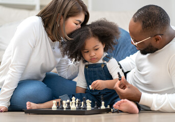 Cute little girl playing chess board as her father sitting by. Multiracial family happy leisure...