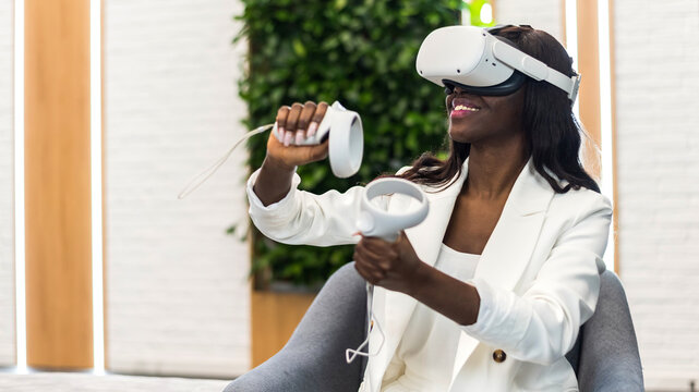 A black woman exploring virtual reality using VR glasses and controllers in an office