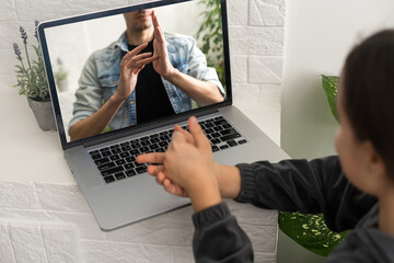 Smiling teenage girl deaf disabled child school girl learning online class on laptop communicating with teacher by video conference call using sign language showing hand gesture during virtual lesson.