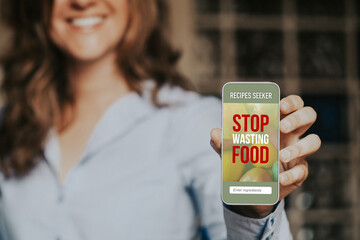 Smiling woman holding a mobile phone with Stop Wasting Food message in the screen.