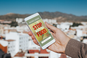 Man holding a mobile phone with Stop Wasting Food message and recipes seeker app in the screen.
