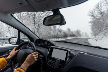View from the car on the countryside winter road. Wide angle image. Hands of a female driver on the steering wheel. Winter road trip concept
