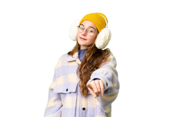 Teenager girl wearing winter muffs over isolated chroma key background points finger at you with a confident expression