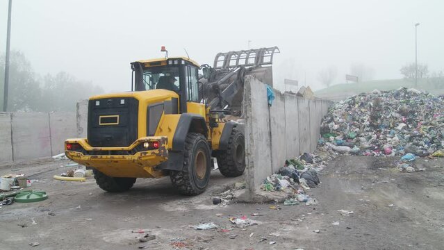 Front loader with scrap handling grapple bucket moving forward and backward to push, scoop and dump material at recycling and waste center, close up view.