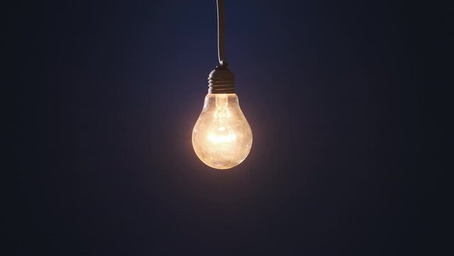Classic lamp glows and flickers on dark blue background. Edison light bulb slowly turned on and off, pulsing light close-up. Warm flashing filament. Vintage Incandescent bulb. Idea, copy space. 4K