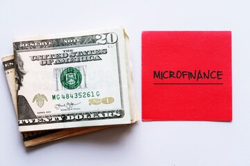 Cash Dollars money and red note with text written MICRO FINANCE , A banking service provided to unemployed or low-income individuals , groups who no access to traditional financial loan
