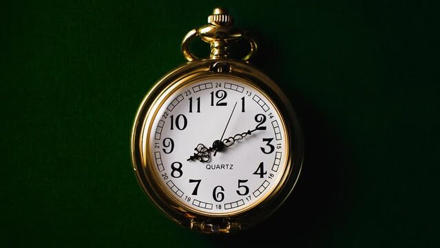 A gold quartz crystal pocket watch lying on dark green fabric. Time lapse of a clock.