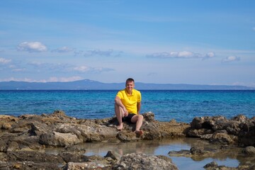 A man in a yellow T-shirt against the background of the sea coast. Sunny weather.