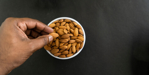 Hand picking up almond top view isolated on black background, copy space image