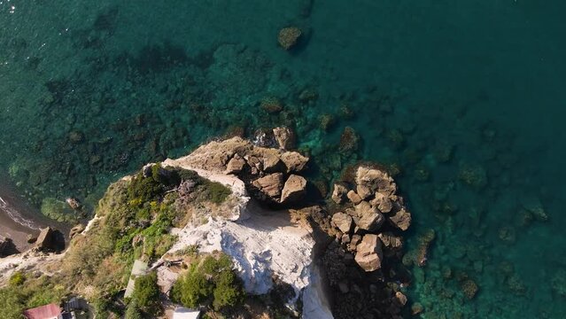 Top down drone shot of a rock formation on the coast of the island of Ischia in Italy with waves crashing onto the beach shot in 4k.