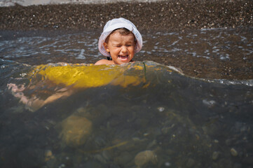 Baby boy swims in a yellow inflatable circle in the sea. The child is happy and laughing.