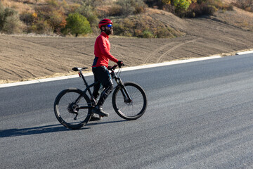 Obraz premium Cyclist riding bicycle on road against clear sky. A man in an outfit stands with a bicycle on an autumn sunny day.