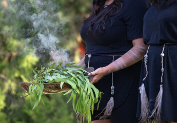 Australian Aboriginal smoking ceremony, woman’s hands are holding burning eucalyptus branches,...