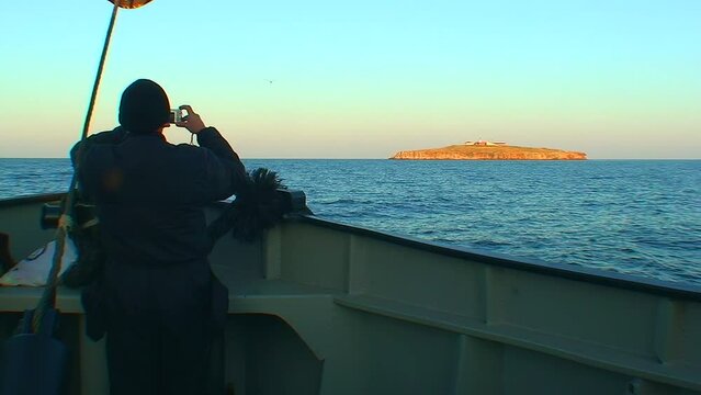 A man with a digital camera stands at the bow of the ship and takes pictures of Snake Island on the horizon. Black Sea, Ukraine.