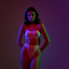 Young woman with slim fit body posing over dark studio background in neon filter light. Night life....