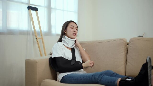 Woman suffered pain from accident fracture broken bone injury with leg splints in cast, neck splints collar, arm splints, sling support arm in living room. Social security and health insurance.
