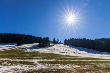 The sun shines from a blue sky over a ski lift that is out of service due to lack of snow near...