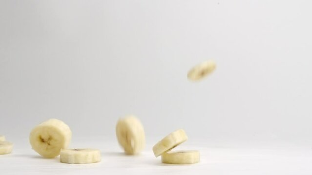 Sliced banana pieces falling onto white table top and landing in a pile in slow motion