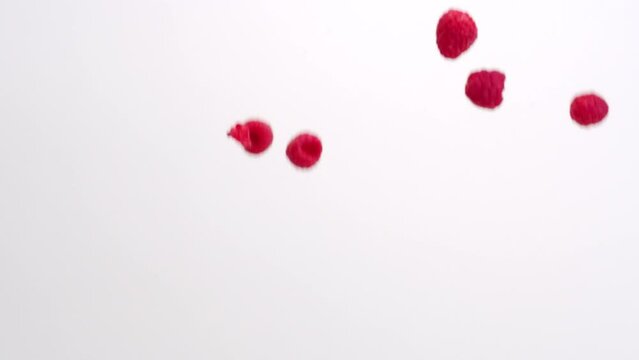Fresh juicy red raspberries raining down on white backdrop in slow motion