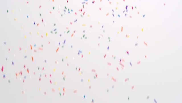 Bright colorful rainbow sprinkle ice cream topping raining down on white backdrop in slow motion