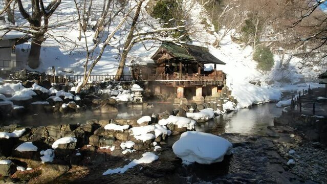 A drone fly towards the natural Hot Spring of Takaragawa Onsen in Gunma, Japan, near a beautiful river in winter during sunrise