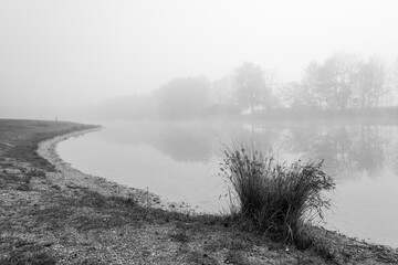 Germeringer See near Germering in Upper Bavaria. Landscape at the lake in the fog. Black and white shot. Foggy morning in nature.
