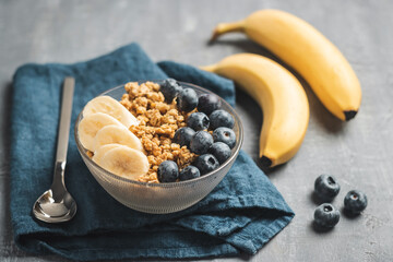 Granola cereal oatmeal with blueberries and banana fruits in a bowl on a grey background
