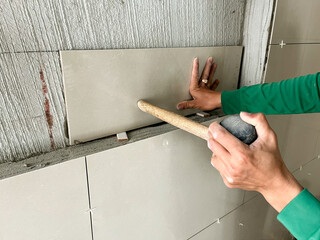 A tiler is tiling a bathroom wall.