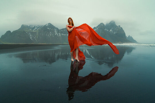 Pretty woman with waving cape on Reynisfjara beach scenic photography. Picture of person with hills on background. High quality wallpaper. Photo concept for ads, travel blog, magazine, article