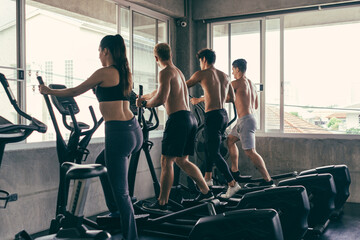 Group of young sporty people doing exercises on elliptical machine at gym. Healthy active lifestyle. Training for muscular body.