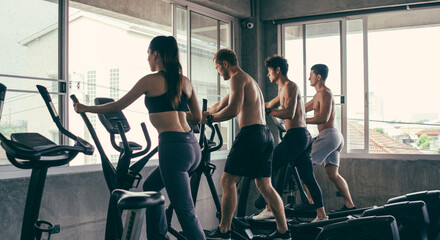 Fototapeta na wymiar Group of young sporty people doing exercises on elliptical machine at gym. Healthy active lifestyle. Training for muscular body.