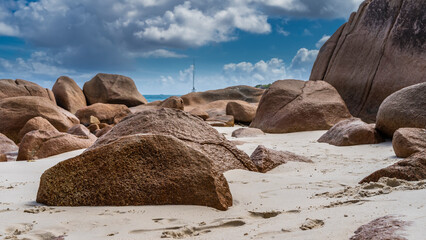 Weathered granite boulders are piled on a tropical beach. Footprints in the sand. Turquoise ocean...
