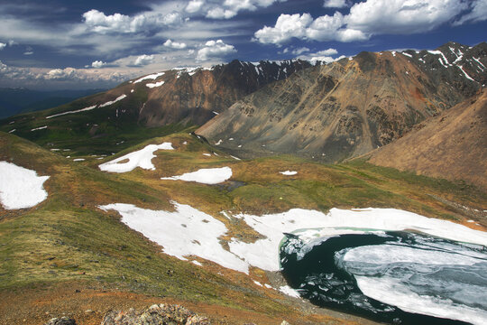 Frozen highland lake among dramatic mountain rocks with snow under blue sky Altai Siberia Russia