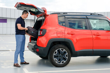 Young man puts a suitcase in the car in the parking lot. People lifestyles and transportation concept