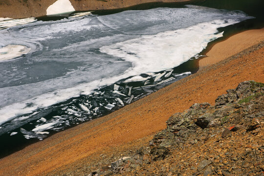 Frozen highland lake among dramatic mountain red and orange rocks with snow Altai Siberia Russia