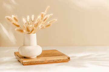 Ceramic vase with lagurus grass on the wooden stand with copy space for home product presentation, warm cozy sunlight and shadows. Scandinavian home interior decoration