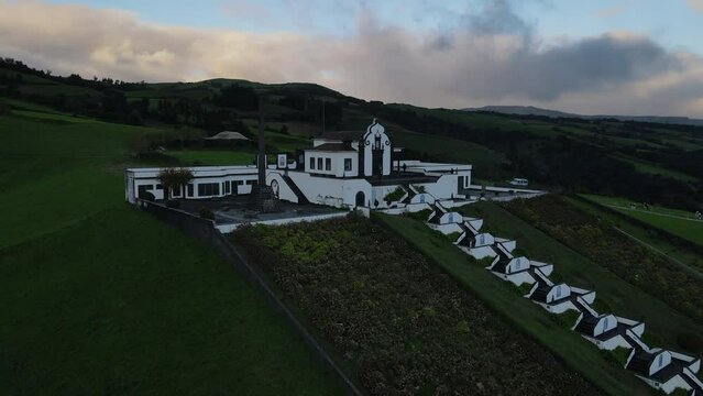 Aerial shot in orbit at medium distance and at sunset over the Chapel of Our Lady of Peace and the large crucifix near the chapel. On the island of Sao Miguel, Azores.