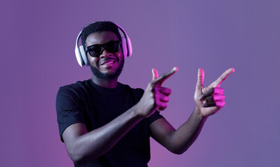 Young African American man in sunglasses and headphones listens to music and dances.