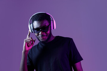 Young African American man in sunglasses and headphones listens to music and dances.