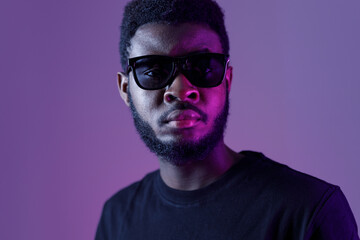 Stylish african american man in sunglasses and on dark neon background.