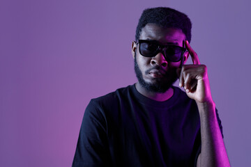 Stylish african american man in sunglasses and on dark neon background.