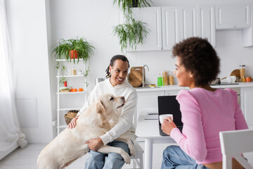 Positive african american couple with labrador talking in kitchen in morning.