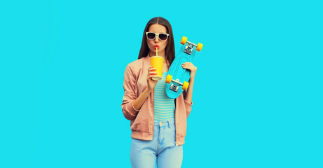 Portrait of stylish young woman with skateboard drinking juice on blue background © rohappy