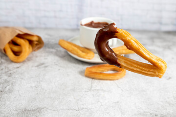 Churro dipping into a cup of hot chocolate on gray stone background, typical Spanish breakfast close up

