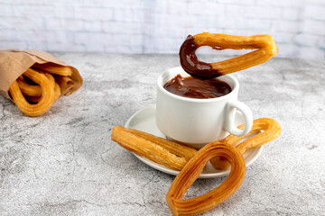 Churro dipping into a cup of hot chocolate on gray stone background, typical Spanish breakfast
